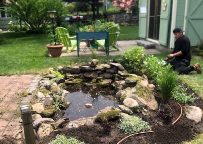 This fun project in Hudson, NH had the crew revisiting and revamping one of our existing gardens! The Excavator dug out 10 yards of poor soil and replaced it with 10 yards of good soil. Last year , in early July, we planted 100 perennials of which half were shade and the others sun loving. These new 80 perennials really made the front side and back yard pond garden quite lovely.