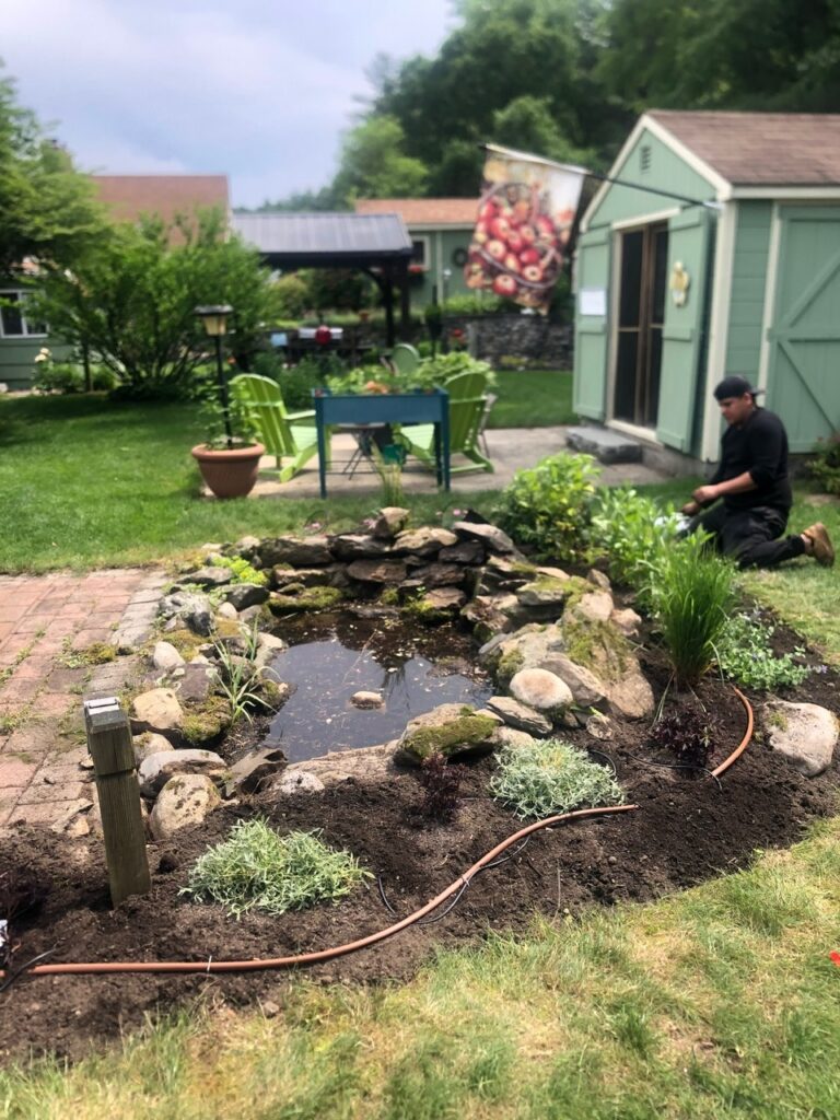 This fun project in Hudson, NH had the crew revisiting and revamping one of our existing gardens! The Excavator dug out 10 yards of poor soil and replaced it with 10 yards of good soil. Last year , in early July, we planted 100 perennials of which half were shade and the others sun loving. These new 80 perennials really made the front side and back yard pond garden quite lovely.